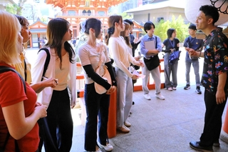 永山広大さん（右端）から英語で生田神社の説明を受ける大学生ら＝神戸市中央区下山手通１