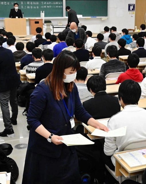 マスク姿で受験生に試験用紙を配る試験官＝１６日午前、神戸市東灘区岡本８、甲南大岡本キャンパス（撮影・中西幸大）