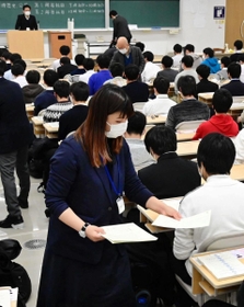 マスク姿で受験生に試験用紙を配る試験官＝１６日午前、神戸市東灘区岡本８、甲南大岡本キャンパス（撮影・中西幸大）