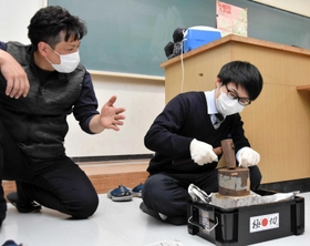 田中誠貴さん（左）の指導を受けながら鍛造の模擬体験をする生徒＝吉川高校