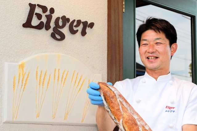 昨春に移転したアイガー加東店でもち麦パンを持つ西嶋直也さん＝加東市上中１