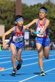 男子・三木東の３区浦井蒼太選手（左）にたすきをつなぐ２区石井颯亜選手＝加古川市西神吉町鼎、加古川運動公園陸上競技場（撮影・笠原次郎）