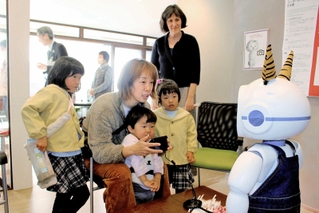 対話ロボットとクイズを楽しむ親子と開発者の１人、インディアナ大のシャバノビッチ教授（右後ろ）＝三木市自由が丘東１、たかはしさんち
