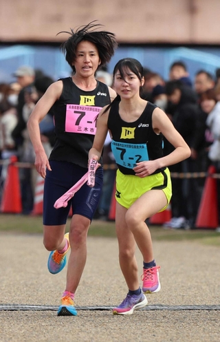 女子・三木市の１区横田歩選手（左）からたすきを受ける２区屋敷萌子選手＝加古川河川敷マラソンコース（撮影・笠原次郎）