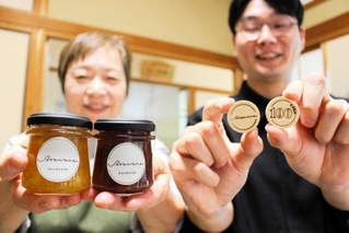 教育支援のためのＳコイン（右）と、コインがもらえる特製ジャム。右は山田勇人さん、左は岡本富恵さん＝三木市宿原、おうちごはんカフェそらまめ