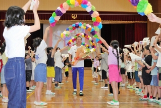 パリ五輪に向かうセルオド・バトオチル選手を花輪のアーチで送り出す児童ら＝緑が丘小学校