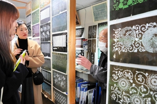 筒井俊雄さん（右）から三木の染め型紙の特徴を聞く喜多方市の木幡江里子さん（左端）とデザイナーの江畑芳さん＝三木市大塚２、ギャラリー湯の山みち