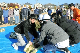 負傷者役の住民を毛布を使って運ぶ訓練に取り組む地域住民ら＝自由が丘中央公園