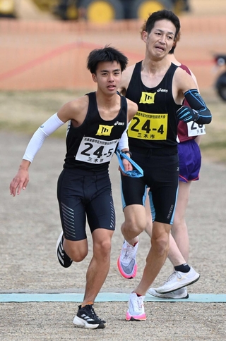 男子・三木市の４区西村教行選手（右）からたすきを受け取る５区北村拓斗選手＝加古川市の加古川河川敷マラソンコース（撮影・斎藤雅志）