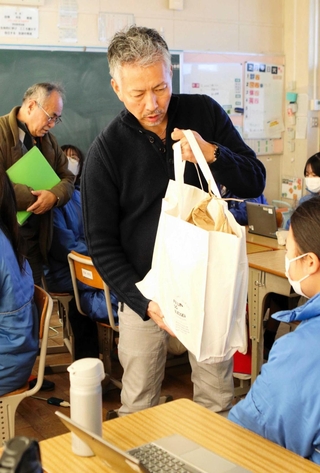 １億円の紙幣と同じ重さのバッグを生徒に渡し、体感させる学校運営協議会の委員ら＝自由が丘中学校