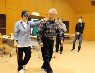 アイマスクを着けたブラインド役を誘導する参加者ら＝三木市末広１