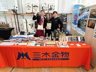 クロミエ市で開催された農業祭で、三木市のブースを出展した同市縁結び課の清水暁彦主幹（左）ら（三木市提供）