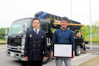 初期消火に貢献し、感謝状が贈られた中島昴さん（右）と、消火に使ったコンクリートポンプ車＝三木市福井、三木市消防本部