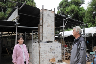 森林に囲まれた土地に再建した窯を見守る坂口忠則さん（右）＝神戸市西区神出町北