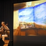 絵本の読み聞かせに合わせてギターを演奏する小巻健さん。平和を求める言葉と音色が響いた＝市立市民活動センター