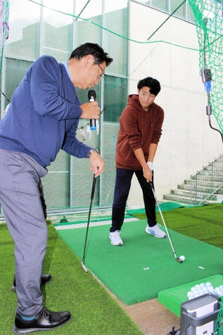 日本ゴルフツアー機構の小山和顕事務局長（左）にアイアンのスイングを教わる大学生＝関西国際大