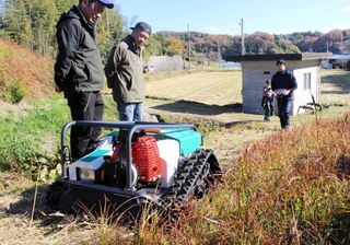 リモート操縦できる草刈り機のデモンストレーションを見学する住民ら＝三木市吉川町上中