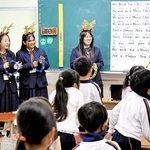 トナカイの角を付けて子どもたちとクリスマスソングを歌う高校生＝平田小学校