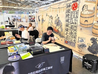 三木金物の歴史と伝統をユニークに紹介するタペストリーを背景にした実演ブース＝７月、パリ（岡田達郎さん提供）