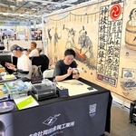 三木金物の歴史と伝統をユニークに紹介するタペストリーを背景にした実演ブース＝７月、パリ（岡田達郎さん提供）