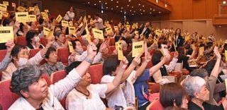 採決時に議決書を掲げるコープこうべの総代たち＝神戸市中央区港島中町６、神戸ポートピアホテル