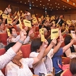 採決時に議決書を掲げるコープこうべの総代たち＝神戸市中央区港島中町６、神戸ポートピアホテル