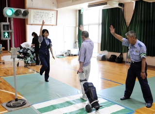 明石署員の補助を受けながら模擬道路の交差点を手を上げて渡る生徒＝明石市大久保町大窪