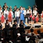 丘みどりさん（舞台中央）とともに、宍粟市歌「ここがふるさと」を披露する吹奏楽団と合唱団の団員ら＝山崎文化会館