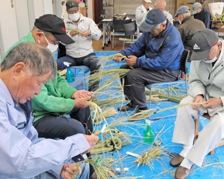 手作業で稲わらを締め上げ、しめ縄を作る参加者たち＝播磨町二子