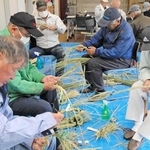 手作業で稲わらを締め上げ、しめ縄を作る参加者たち＝播磨町二子