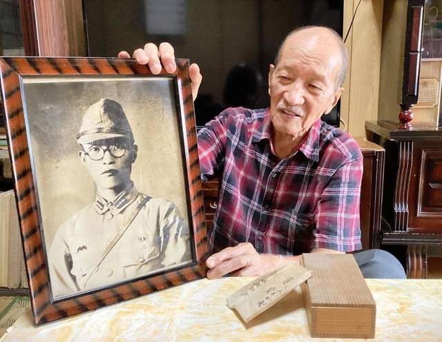父恒男さんの遺影を手に、「戦犯遺族」としての思いを語る寺越脩さん＝西脇市岡崎町