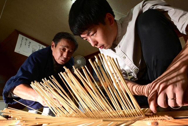 真剣なまなざしで柳行李を編む田中皓之さん（右）。師匠の寺内卓己さんが傍らで見つめ、助言を送る＝豊岡市出石町魚屋、たくみ工芸