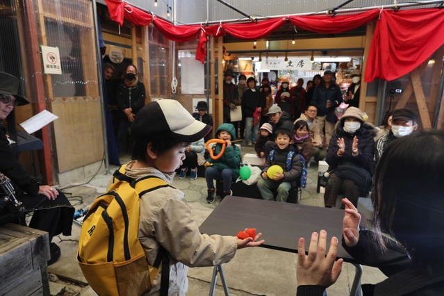 「防災空地」で開かれるＴＯＭＡＺ（とまつ）さん（手前右）らのマジックショーは定番に。バンドの生演奏に合わせて不思議な技が繰り広げられ、子どもも大人も歓声を上げた＝神戸市灘区水道筋３