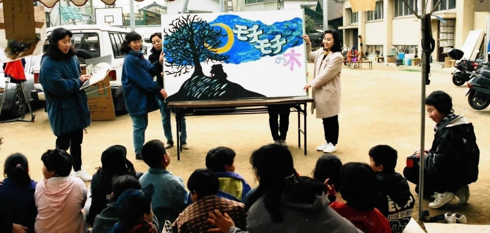 避難所の子どもたちに、手作りの大きな絵本を見せるボランティアたち＝１９９５年２月、神戸市長田区