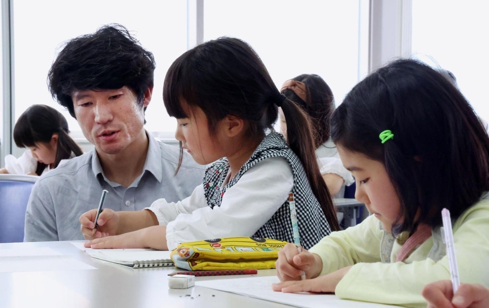 感想文を書く子どもたちの様子を見守る長谷川元気さん（左から２人目）＝４月６日、神戸新聞社