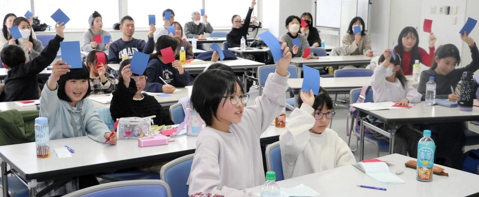 防災ゲーム「クロスロード」でカードを上げる子どもたち＝神戸新聞社