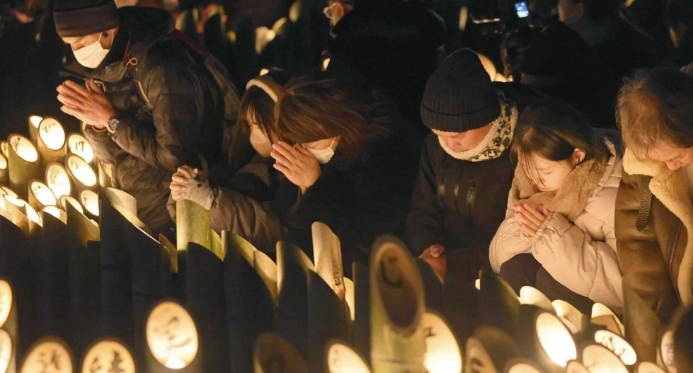 竹灯籠の前で手を合わせる人たち＝２０２５年１月１７日午前５時４６分、神戸市中央区、東遊園地