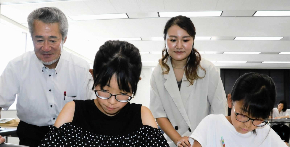 感想文を書く児童を見守る米山正幸さん（左）と未来さん（左から３人目）＝神戸市中央区東川崎町１、神戸新聞社