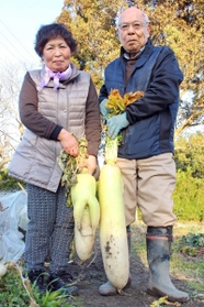 脚が隠れるサイズの巨大大根（右）とお化けのような手が付いた大根を持つ大西さん夫妻＝三田市四ツ辻