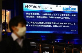 ２月２日に緊急事態宣言の延長決定のニュースを伝える大型ビジョン前を歩くマスク姿の男性