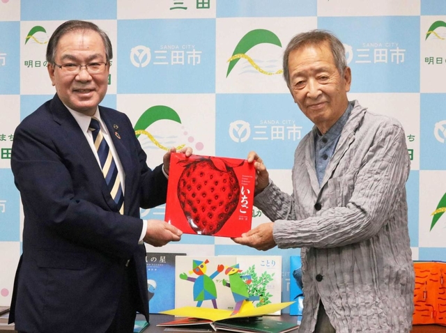 森哲男市長（左）に絵本を手渡す新宮晋さん＝三田市役所