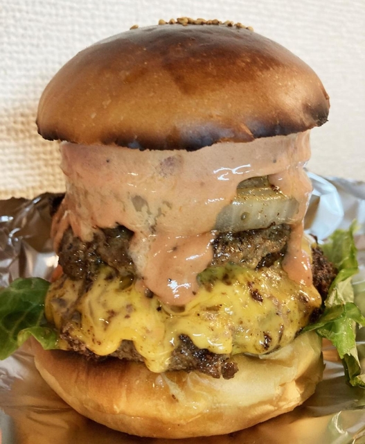 肉厚なパティの間からチーズがあふれ出すハンバーガー（提供）