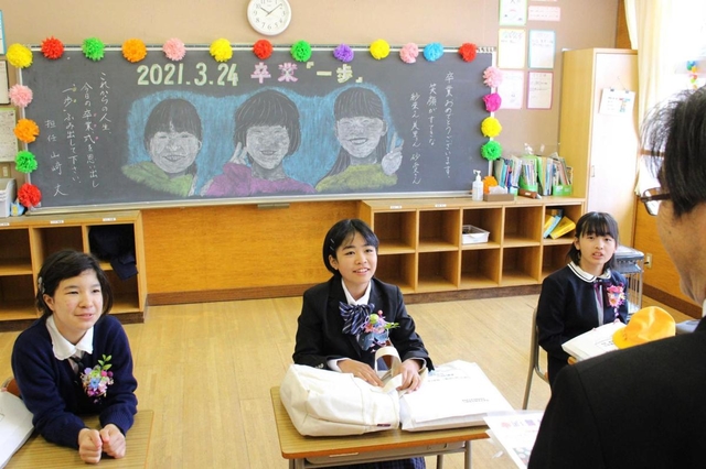 担任の山崎丈教諭が描いた似顔絵を背に思い出を語る卒業生＝母子小学校