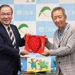 森哲男市長（左）に絵本を手渡す新宮晋さん＝三田市役所