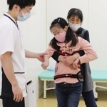 母眞澄さんに抱えられ、脚を前に出す練習をする望美さん＝尼崎市西大物町