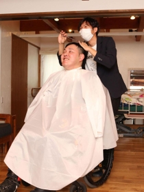 車いすに座った中江卓巳さんをカットする団野圭輔さん＝三田市