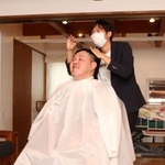 車いすに座った中江卓巳さんをカットする団野圭輔さん＝三田市