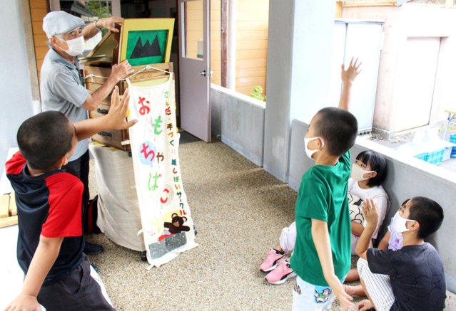 大きく手を上げてクイズに答える子どもたち＝母子小学校