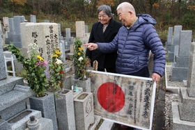 杉尾五郎さんの日章旗を墓前に供える甥の典一さん（右）と三田市遺族会の竹内ハルミさん＝三田市東野上