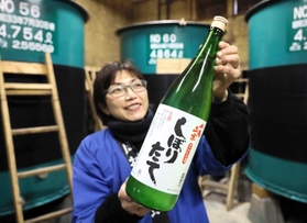 蔵の中で新酒を持つ岡村理恵さん＝岡村酒造場